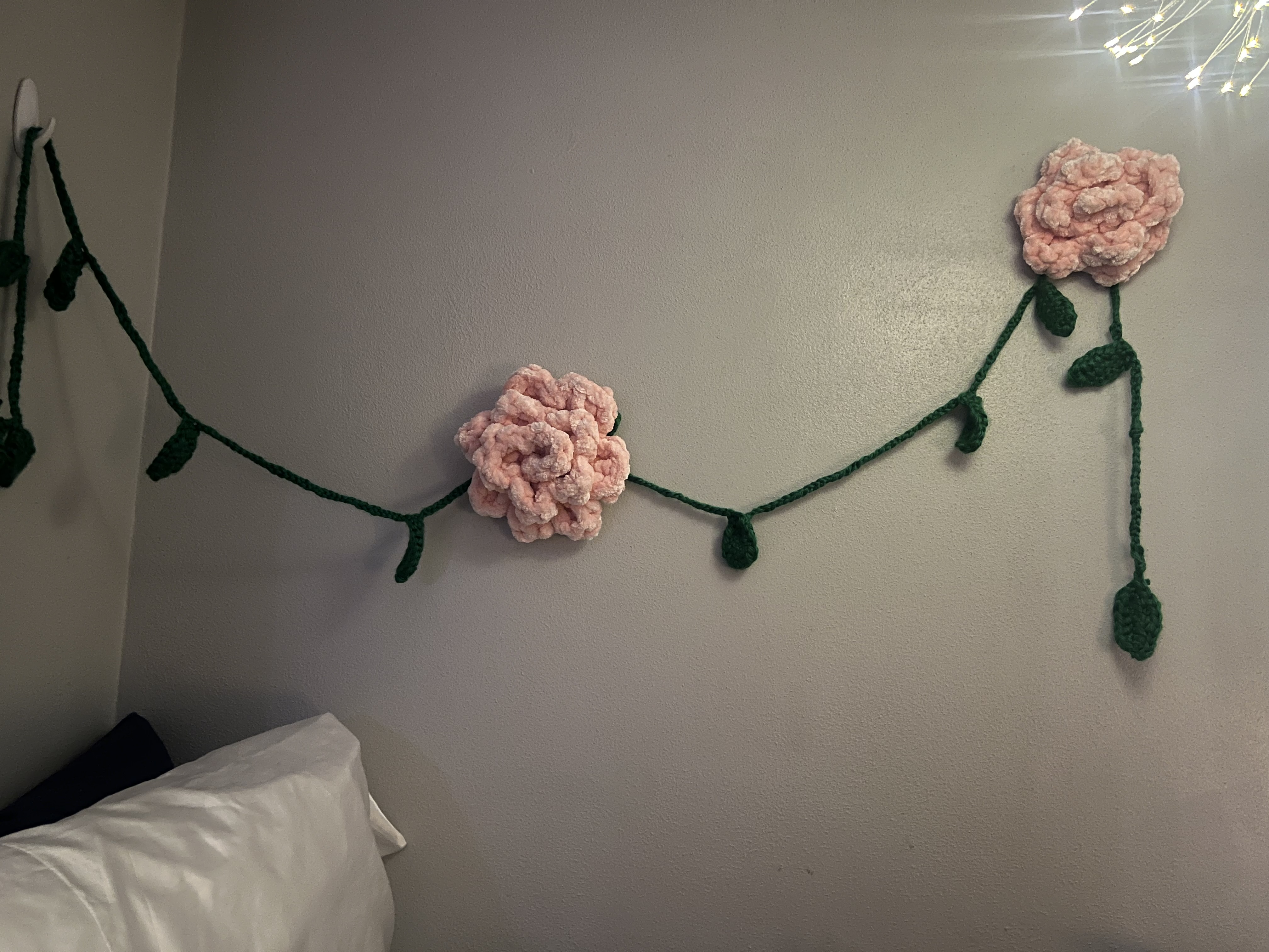 Two fuzzy crochet flowers similar to a rose with a green crochet vine between them.